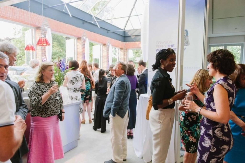 People socialising at an event at William Morris Gallery in the Cafe space. People stand with wine glasses and chat to each other.
