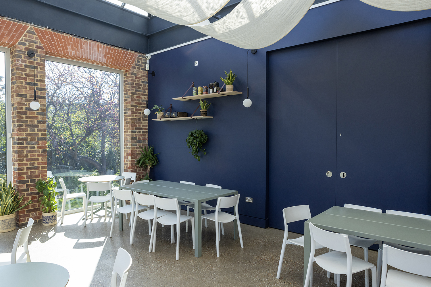 Image of the Cafe at William Morris Gallery. We see tables and chairs, with sun shining in through the glass roof.