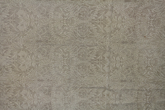Fabric sample featuring a symmetrical ogee pattern of stylised leaves and flowers printed in pale ochre.