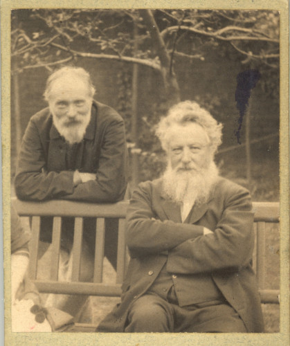 Edward Burne-Jones stands behind William Morris, who is sitting on a bench in the garden at The Grange