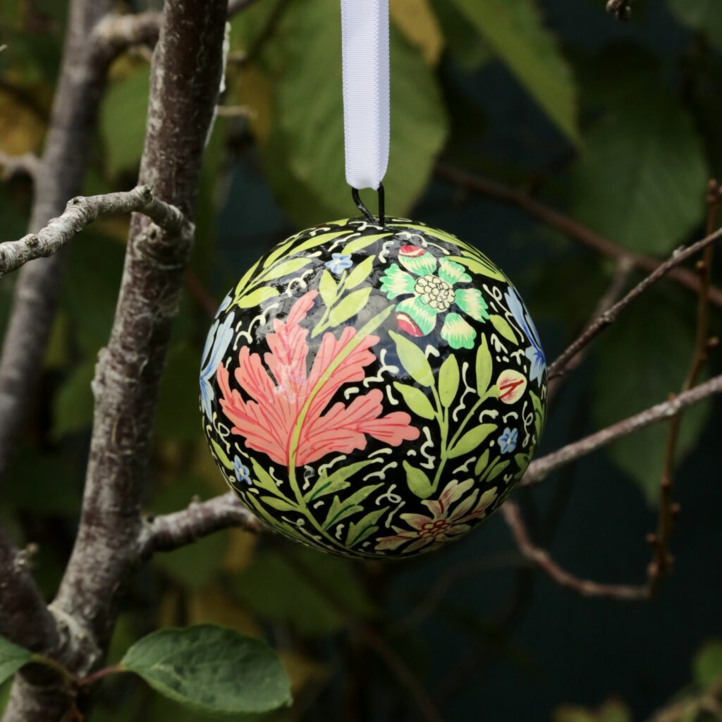 A painted bauble hung from a tree with a leaf pattern