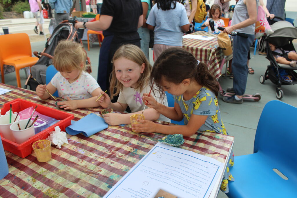 Three children enjoying craft activities on a table outside